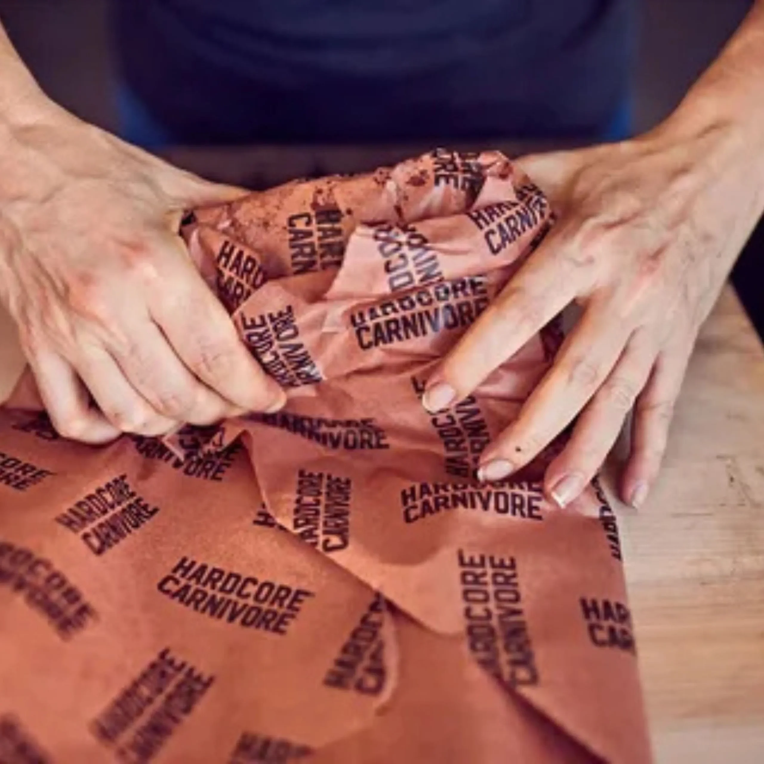 Chef hands wrapping a brisket with pink BBQ butcher paper